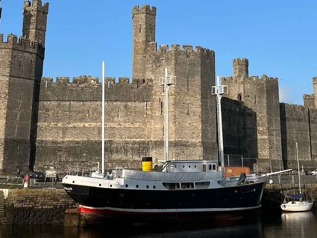 A dark boat docked in front of the massive walls of Caernarfon Castle