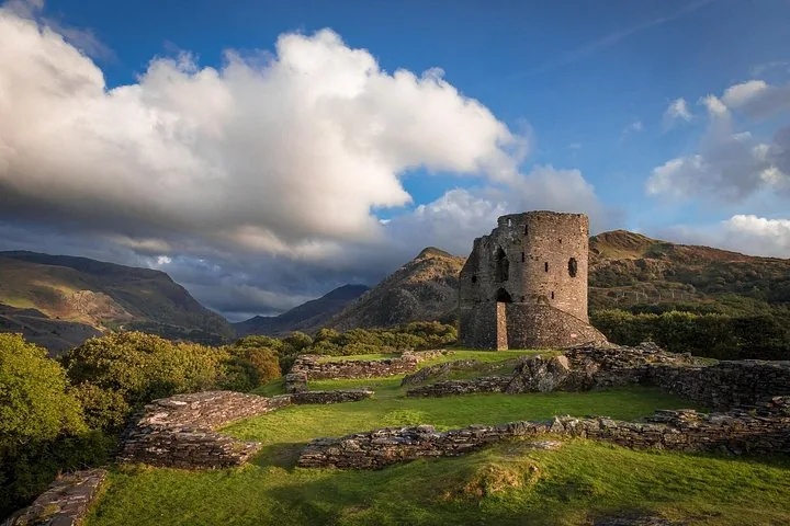 Rovine della torre di un castello in pietra su una collina erbosa con montagne alle spalle