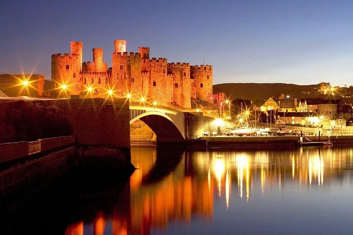 Il Castello di Caernarfon illuminato al tramonto, con una luce arancione riflessa sull'acqua