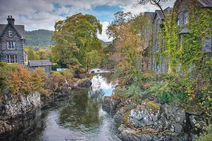 A peaceful river flowing past stone houses with ivy and autumn trees